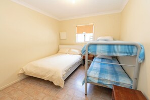 Eine kleine, einfache Unterkunft mit einem Etagenbett, einem Einzelbett, einem Nachttisch und einem Fenster mit Jalousie.