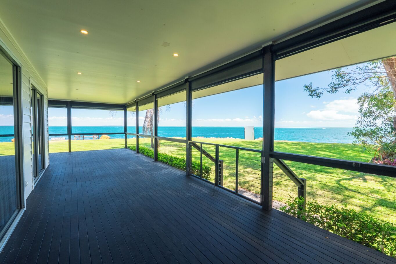 A covered outdoor area with a view of the ocean, wooden flooring, and metal railings.