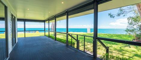 A covered outdoor area with a view of the ocean, wooden flooring, and metal railings.
