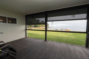 A room with a large sliding glass door leading to a grassy outdoor area with a view of the sea. - Sand Bar - Absolute Waterfront Escape, Amity Point (Amity Point)