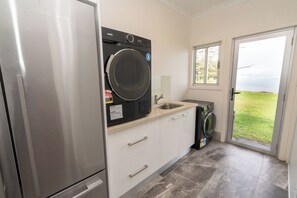 A compact kitchen with a stainless steel refrigerator, a washing machine, and a sink. - Sand Bar - Absolute Waterfront Escape, Amity Point (Amity Point)