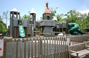 A wooden play structure with multiple slides and climbing areas, surrounded by a wooden fence. - The Best of Both Worlds - Lakefront Views + Private Beachside Resort (Destin)