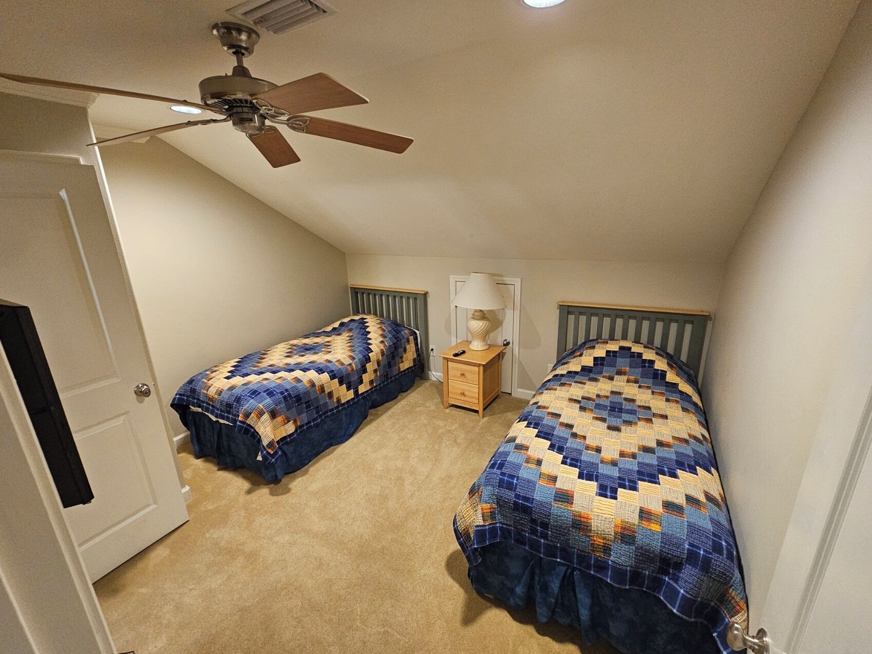 Un dormitorio con dos camas, ventilador de techo, mesita de noche y lámpara.