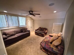 Ein Zimmer mit Deckenventilator, einem braunen Sofa, einem gemusterten Sitzsofa und einer Tür.