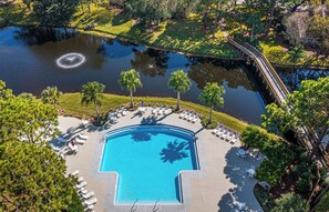 An aerial view of a resort with a swimming pool, lounge chairs, palm trees, and a bridge over a pond. - The Best of Both Worlds - Lakefront Views + Private Beachside Resort (Destin)