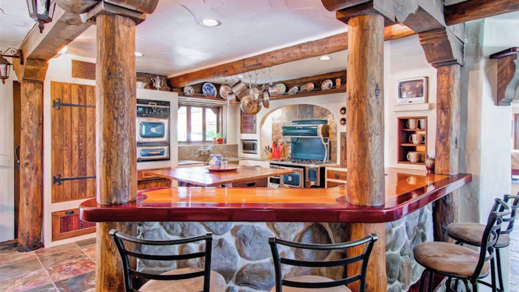 A kitchen with a central island, stone walls, and wooden beams.