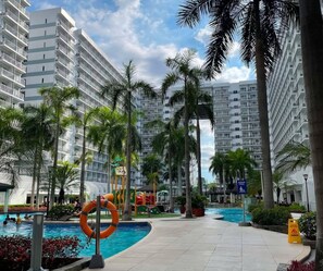 A hotel pool area with a lifebuoy, palm trees, and a kiddie pool. - The Executive Suites - Shell Residences Manila 1BR Condo near MOA NAIA Ikea (Pasay City)