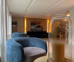 Um hall moderno com balcão de recepção, uma grande pintura abstrata e uma cúpula de vidro singular sobre uma mesa com vela.