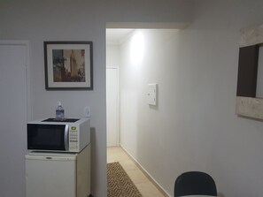 Eine kleine Küchenzeile mit einer Mikrowelle, einem kleinen Kühlschrank und einem Stadtbild im Bilderrahmen an der Wand.