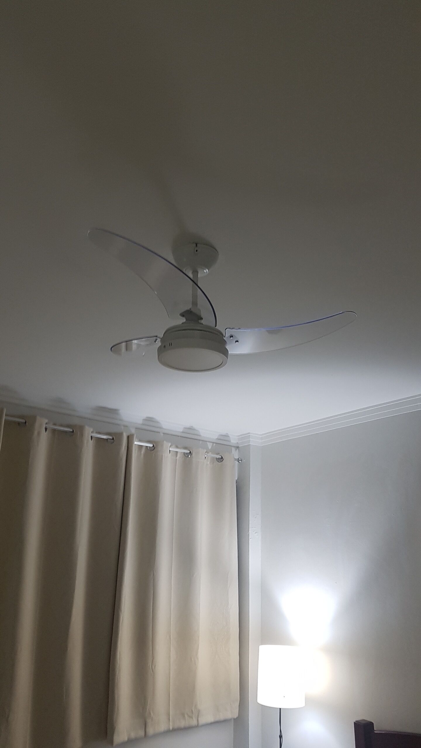 En takfläkt med en lampa, beige gardiner och en vägglampa.