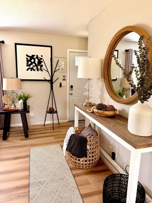 A well-lit room with a wooden floor, a round mirror, a lamp, a framed artwork, and a woven basket. - Modern 2-bedroom house in Beautiful Mount Vernon, Ohio (Mount Vernon)
