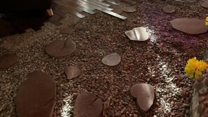A dining area with a wooden table and chairs, a dark leather sofa, and a floor covered with pebbles and flower petals. - casa raizal (Envigado)
