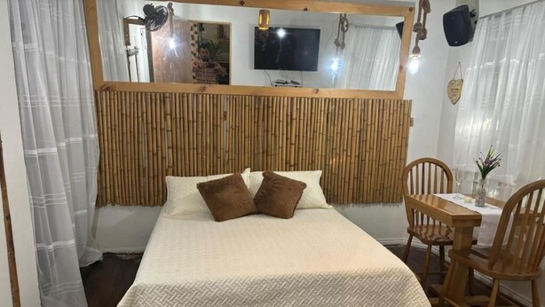 A bedroom with a bed, a wooden headboard, a TV, a small table, and chairs. - casa raizal (Envigado)