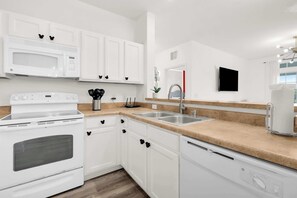 Une cuisine moderne avec des meubles blancs, un four à micro-ondes encastré, une cuisinière et un évier.