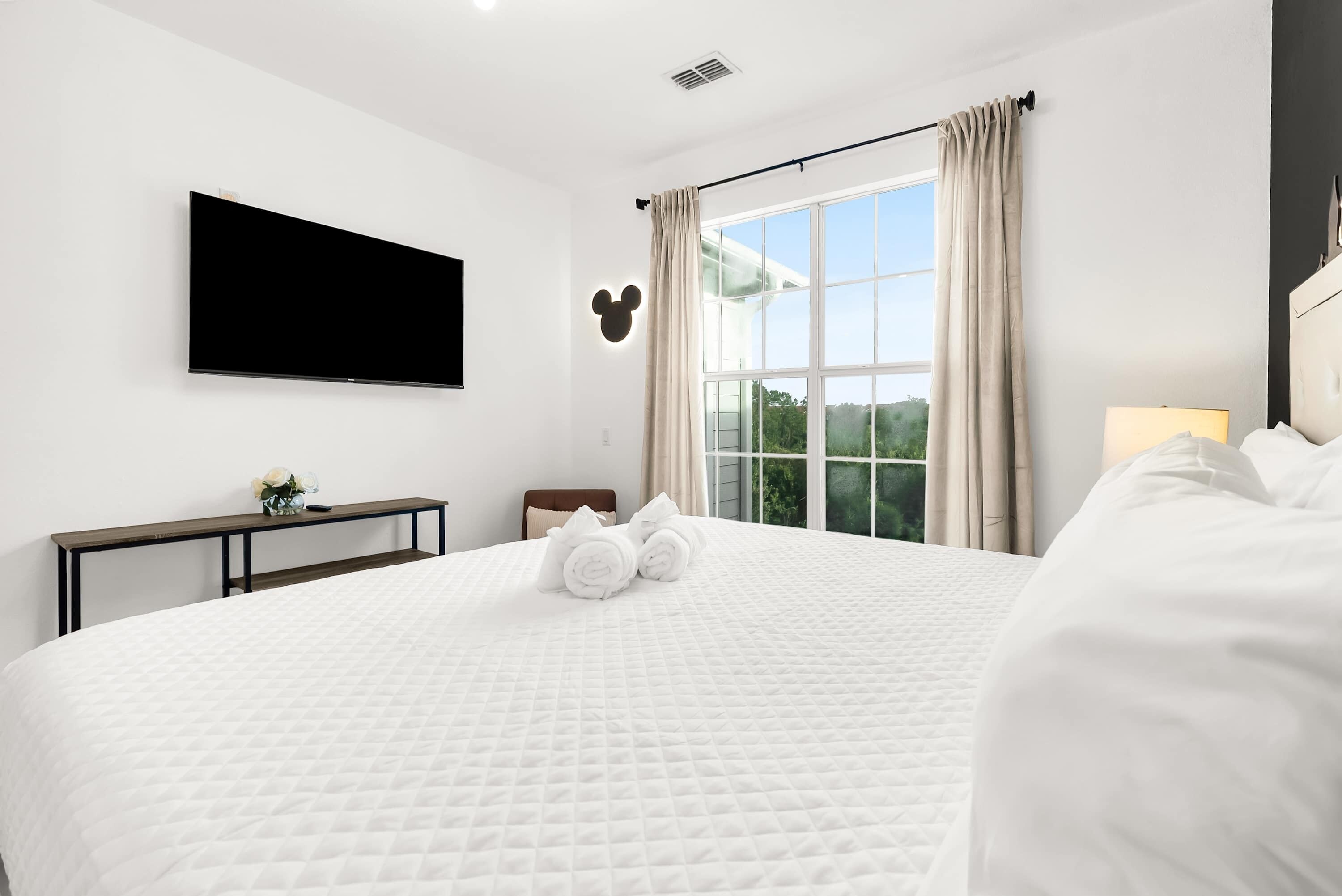 Une chambre d’hôtel avec un grand lit, un téléviseur à écran plat fixé au mur, une fenêtre avec des rideaux et un phare en forme de Mickey Mouse.