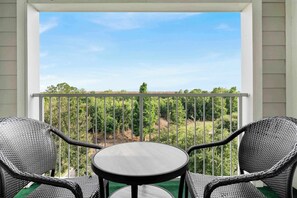 Un balcon avec deux fauteuils en osier et une petite table ronde, donnant sur un vignoble.