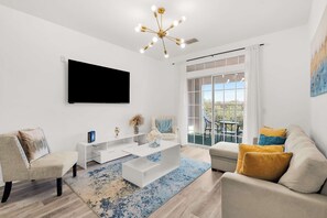 A modern living room with a flat-screen TV, a white coffee table, and a sofa with cushions. - Secret Lake Resort Balcony Retreat (Kissimmee)