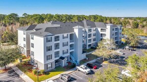 A multi-story apartment building with a central staircase, parking lot, and surrounding greenery. - Secret Lake Resort Balcony Retreat (Kissimmee)
