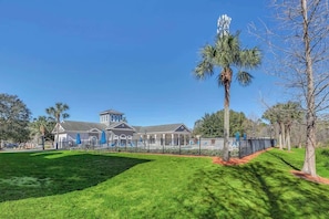 A building with a large lawn, a palm tree, and a fenced playground area. - Secret Lake Resort Balcony Retreat (Kissimmee)