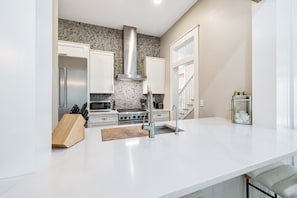 A modern kitchen with white cabinetry, a stainless steel range hood, and a white countertop. - Next to Camp Watercolor and Watercolor Publix (Santa Rosa Beach)