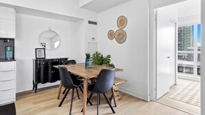 Une cuisine moderne avec une table en bois, des chaises noires, un miroir rond et des œuvres d’art décoratives accrochées au mur.