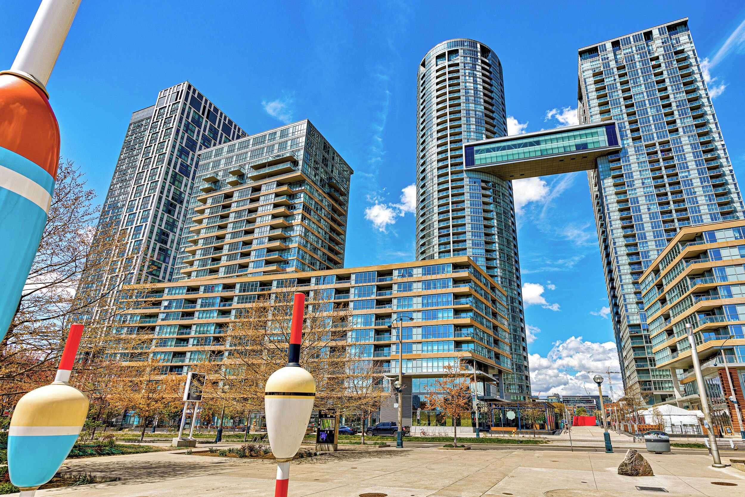 Una zona urbana moderna con edificios altos, un cielo azul despejado y una pasarela para peatones.