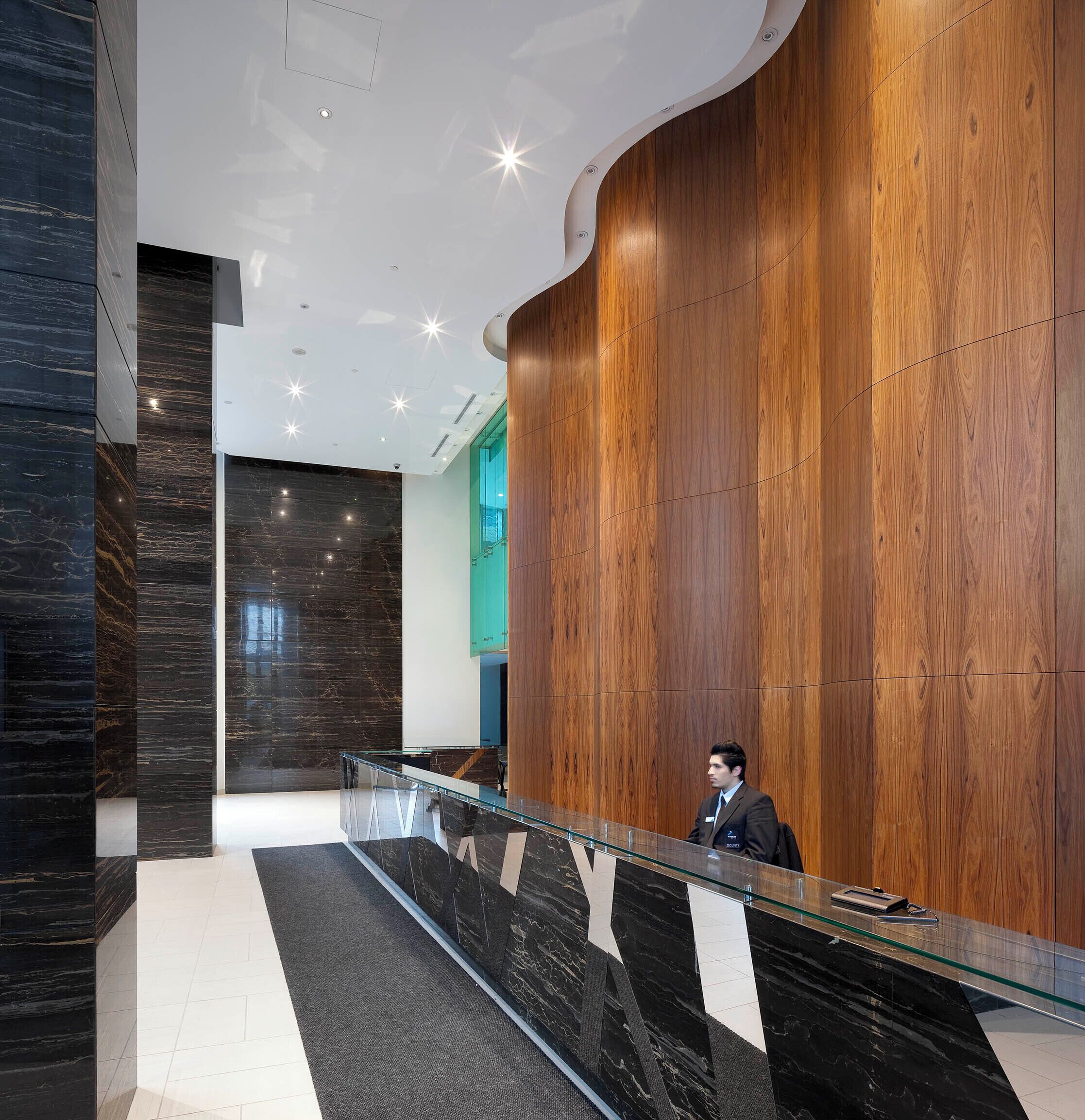 A modern reception area with a glass counter, wooden paneling, and a marble floor.