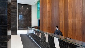 Una moderna zona de recepción con mostrador de vidrio, paneles de madera y suelo de mármol.
