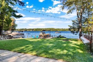 A backyard with a lawn, a dock, boats, and a string of lights.