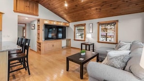 A spacious living area with a wooden ceiling, a sofa, a coffee table, and a TV. - Breakaway Lake House (Northwood)