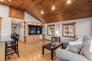 A spacious living area with a wooden ceiling, a sofa, a coffee table, and a TV.