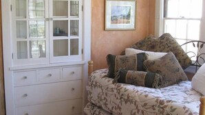Una camera da letto con un letto, una cassettiera, una finestra con tende e un quadro appeso al muro.