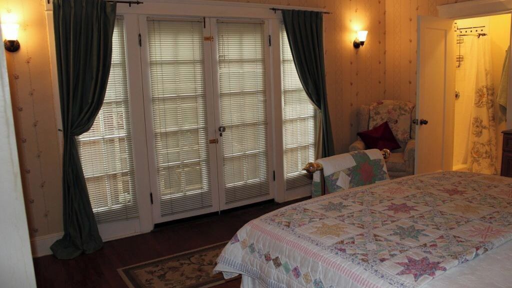 A bedroom with a bed, a chair, a door, and a window with curtains.