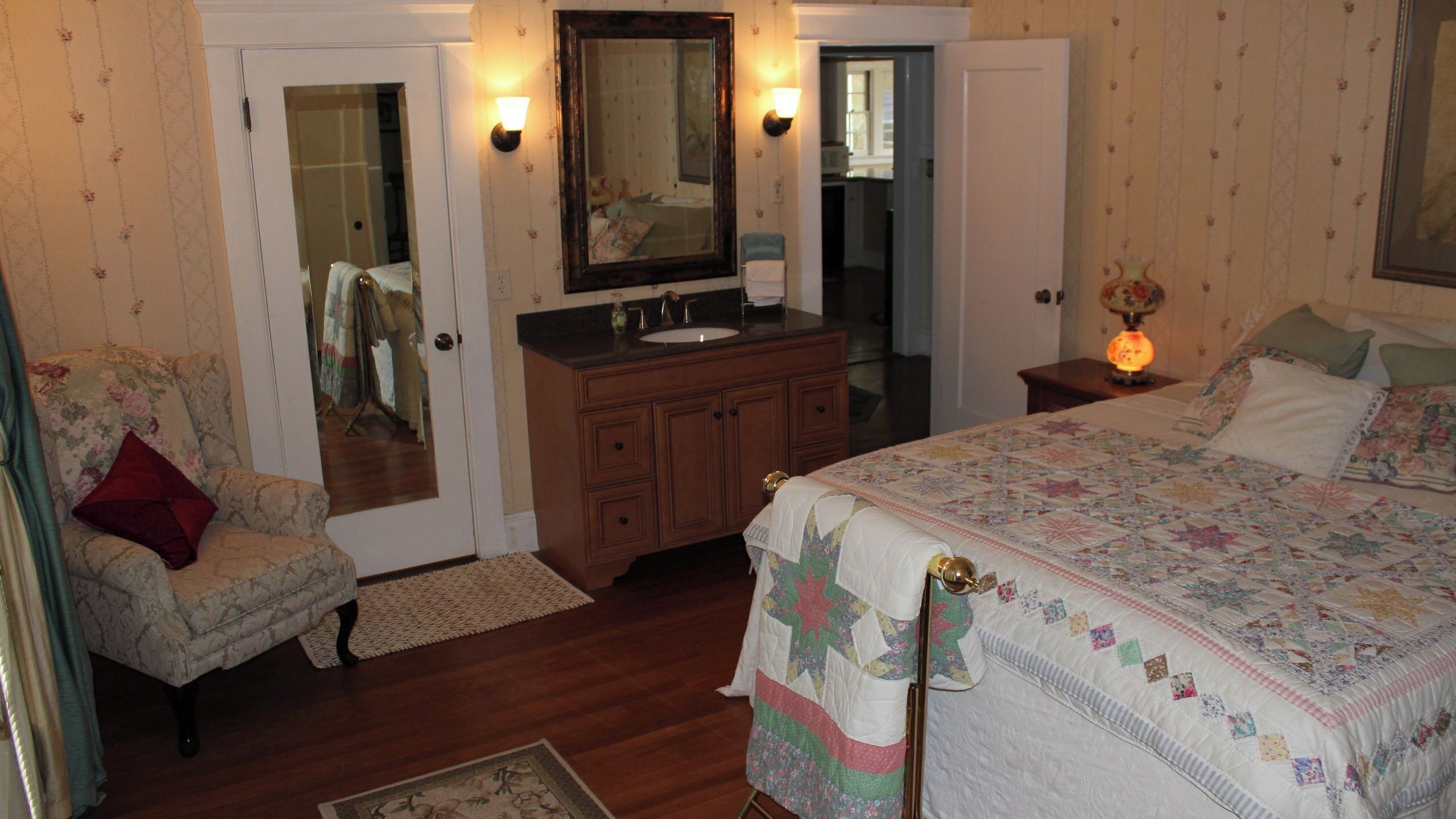 A bedroom with a bed, a chair, a dresser, a mirror, and a nightstand with a lamp.
