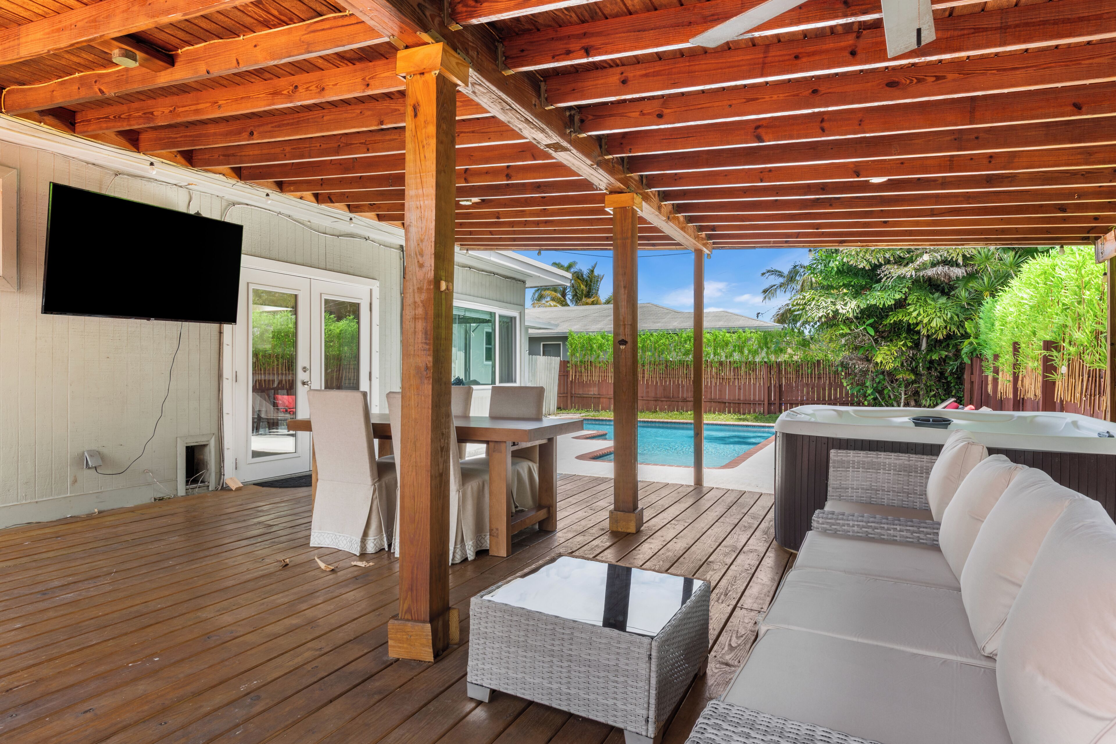 An outdoor deck with a pool, wooden furniture, and a covered area.