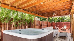A hot tub under a wooden pergola with bamboo, surrounded by a wooden deck, outdoor furniture, and a wooden fence.