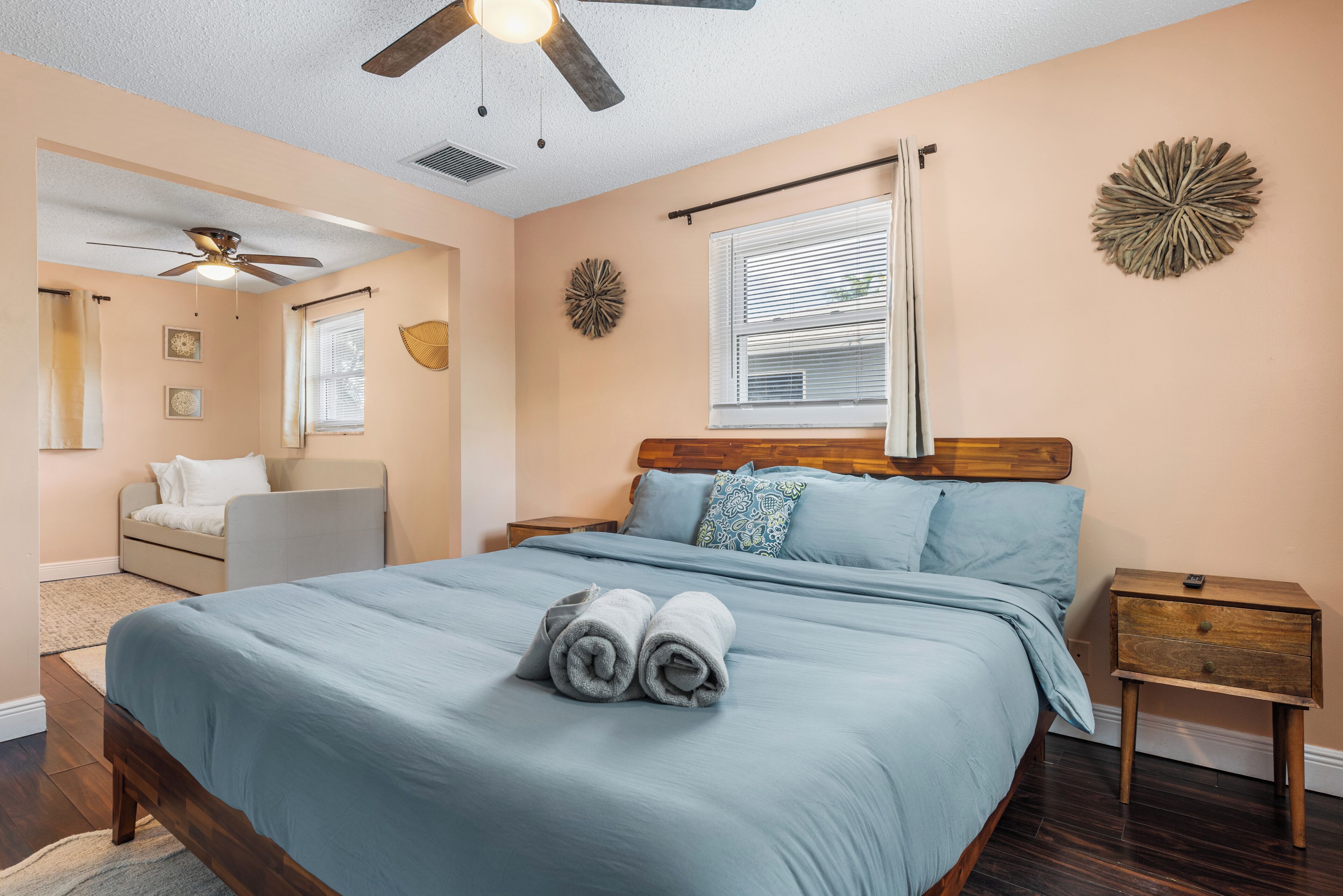 A bedroom with a bed, a nightstand, a ceiling fan, a window with blinds, and a wall decoration.