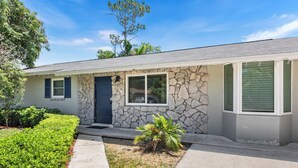A single-story house with a stone facade, a front door, and a small front yard with a palm tree.