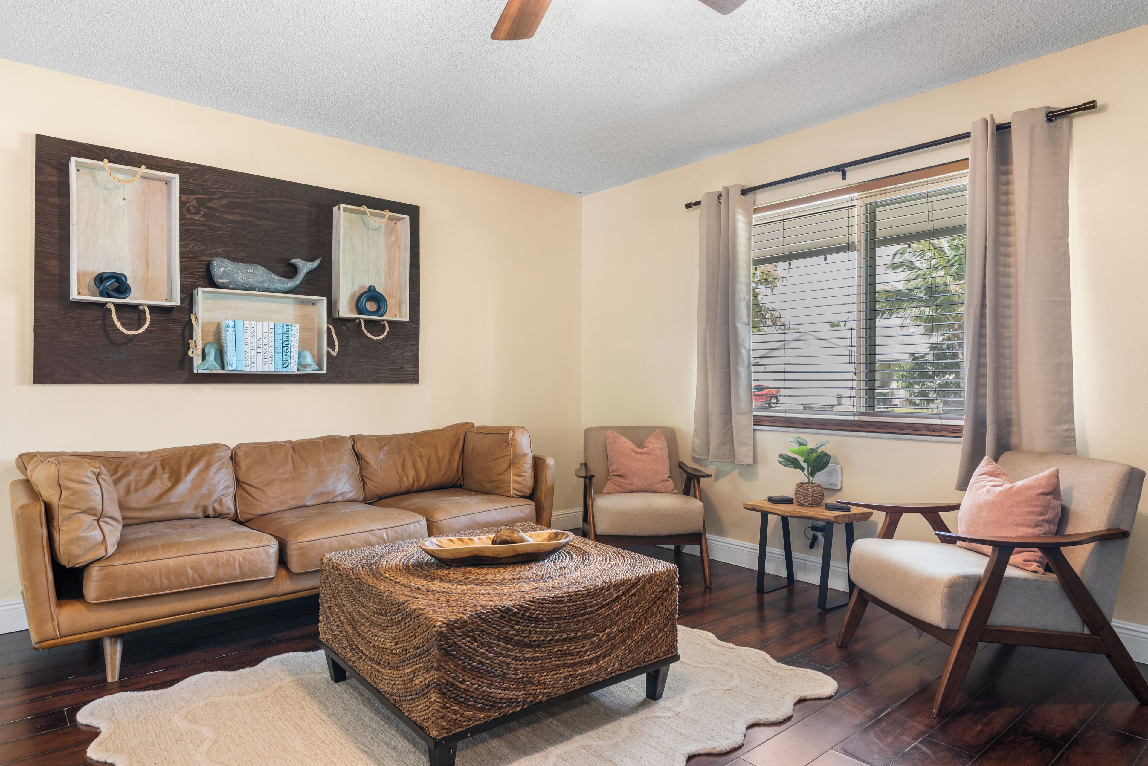 A living room with a brown leather sofa, a woven ottoman, a wooden coffee table, and a small side table with a plant.