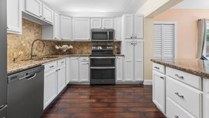 A kitchen with white cabinets, a granite countertop, a built-in microwave, a double oven, and a dishwasher.