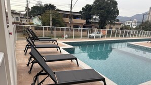 A swimming pool with lounge chairs and a view of residential buildings in the background. - Fully furnished apartment | 1 bedroom | Garage | Dom Bosco - Itajaí (Itajaí)