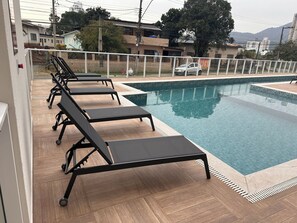 A swimming pool with lounge chairs and a view of residential buildings in the background. - Fully furnished apartment | 1 bedroom | Garage | Dom Bosco - Itajaí (Itajaí)