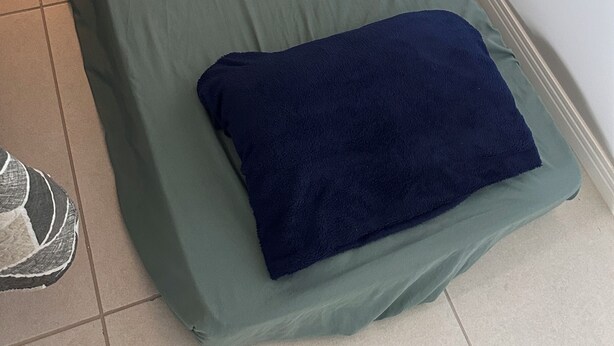 A single bed with a green mattress and a blue blanket, a pillow, and a small bedside table with a lamp. - Fully furnished apartment | 1 bedroom | Garage | Dom Bosco - Itajaí (Itajaí)