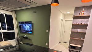 A modern kitchen with a black granite countertop, a bowl of fruit, a built-in oven, and a television mounted on the wall. - Fully furnished apartment | 1 bedroom | Garage | Dom Bosco - Itajaí (Itajaí)