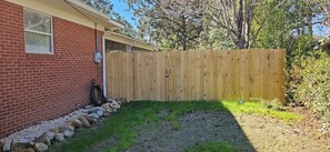 A backyard with a wooden fence, a brick house, and a hose. - Open floor-plan - Large Covered Patio - Kitchen Island - 5 beds (Dothan)