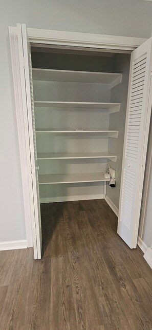 Un dressing accessible sans porte, dont les étagères sont visibles et qui est équipé d’une prise de courant au sol.