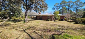 A residential property with a brick house, a covered patio, and a lawn with scattered leaves.