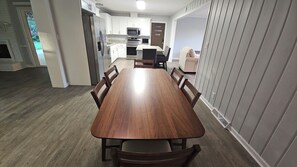 A dining area with a wooden table and chairs, a kitchen in the background, and a view of the outdoors. - Open floor-plan - Large Covered Patio - Kitchen Island - 5 beds (Dothan)