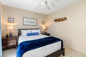 A bedroom with a bed, two bedside tables, a ceiling fan, and wall art. - 🏖️Alii Villas 317 | Sunset Views | Remodeled | Pool & A/C (Kailua Kona)