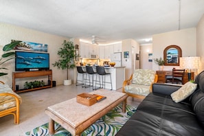 A modern living room with a television, seating, and a kitchen area. - 🏖️Alii Villas 317 | Sunset Views | Remodeled | Pool & A/C (Kailua Kona)